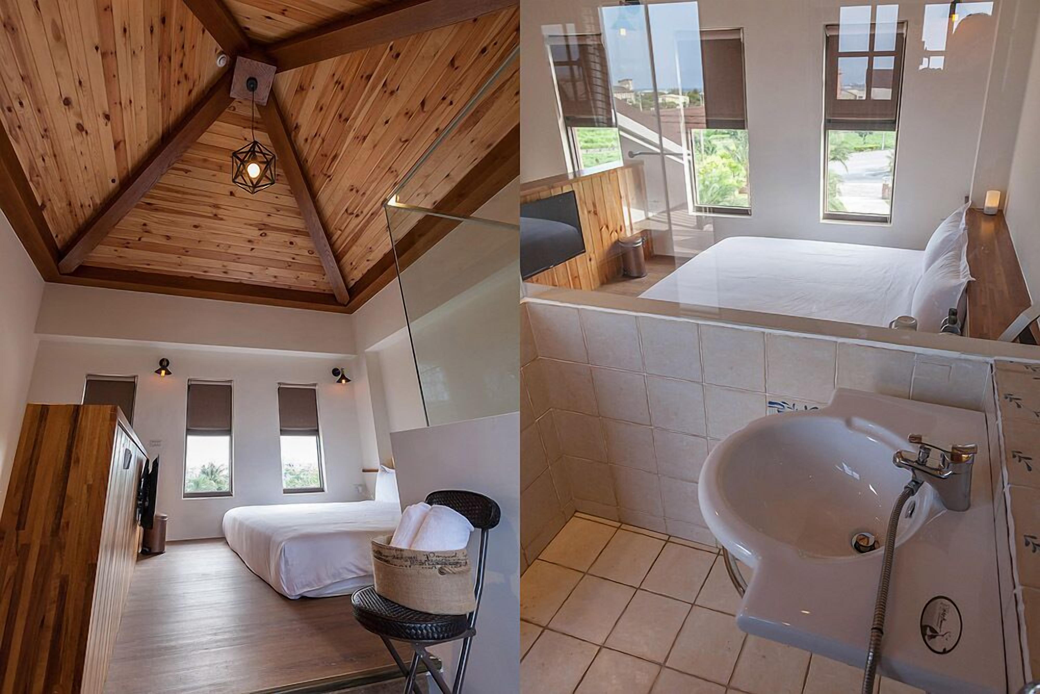 Ein modernes Zimmer mit schrägverdeckter Decke, einem Bett, einem Sessel, einem kleinen Tisch und einem Fenster mit Blick auf Grünflächen.