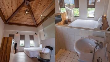 Ein modernes Zimmer mit schrägverdeckter Decke, einem Bett, einem Sessel, einem kleinen Tisch und einem Fenster mit Blick auf Grünflächen.