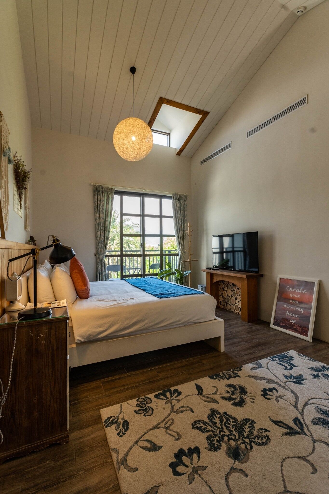 Un dormitorio con una cama grande, televisión, escritorio y ventana con cortinas.