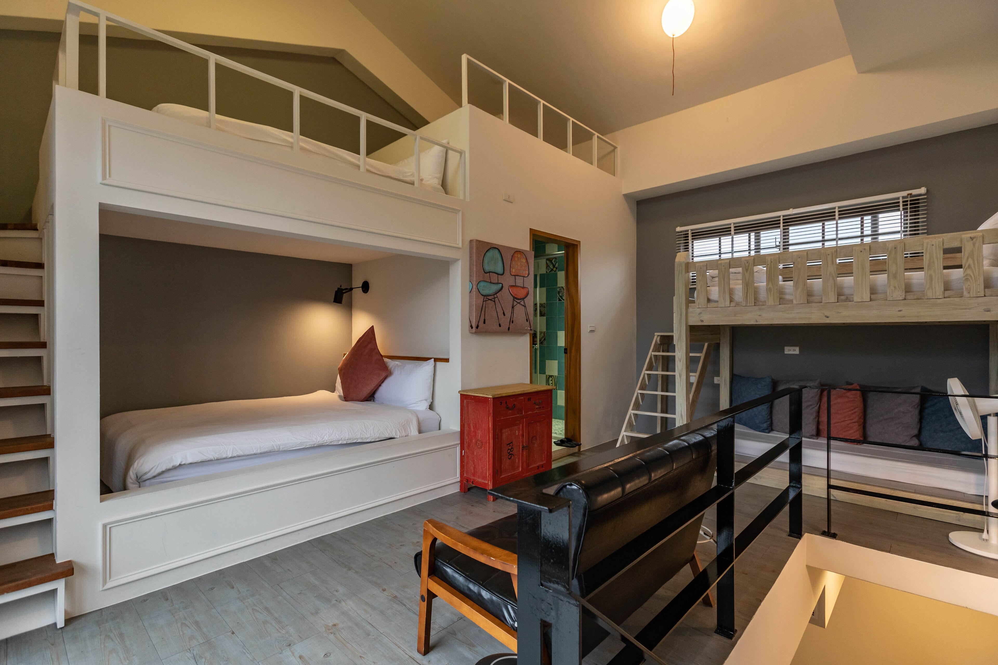 Quarto com beliche de vários níveis, escada, armário vermelho e um banco preto.