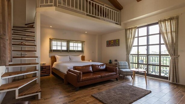 A bedroom with a large bed, a brown leather sofa, a small table, and a staircase. - Forest B&B (Ji'an)