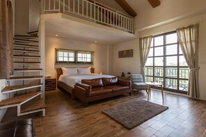 Un dormitorio con una cama grande, un sofá de cuero marrón, una mesita y una escalera.