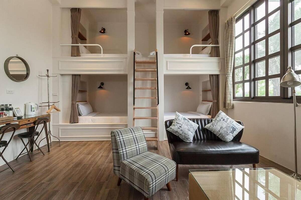 A room with a bunk bed, a desk with a chair, a couch, and a window with curtains.