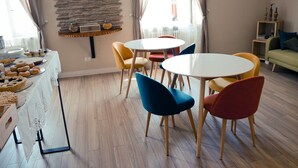 A dining area with round tables and colorful chairs, a buffet with pastries, and a stone wall with a shelf. - Leucos B&B (Potenza)