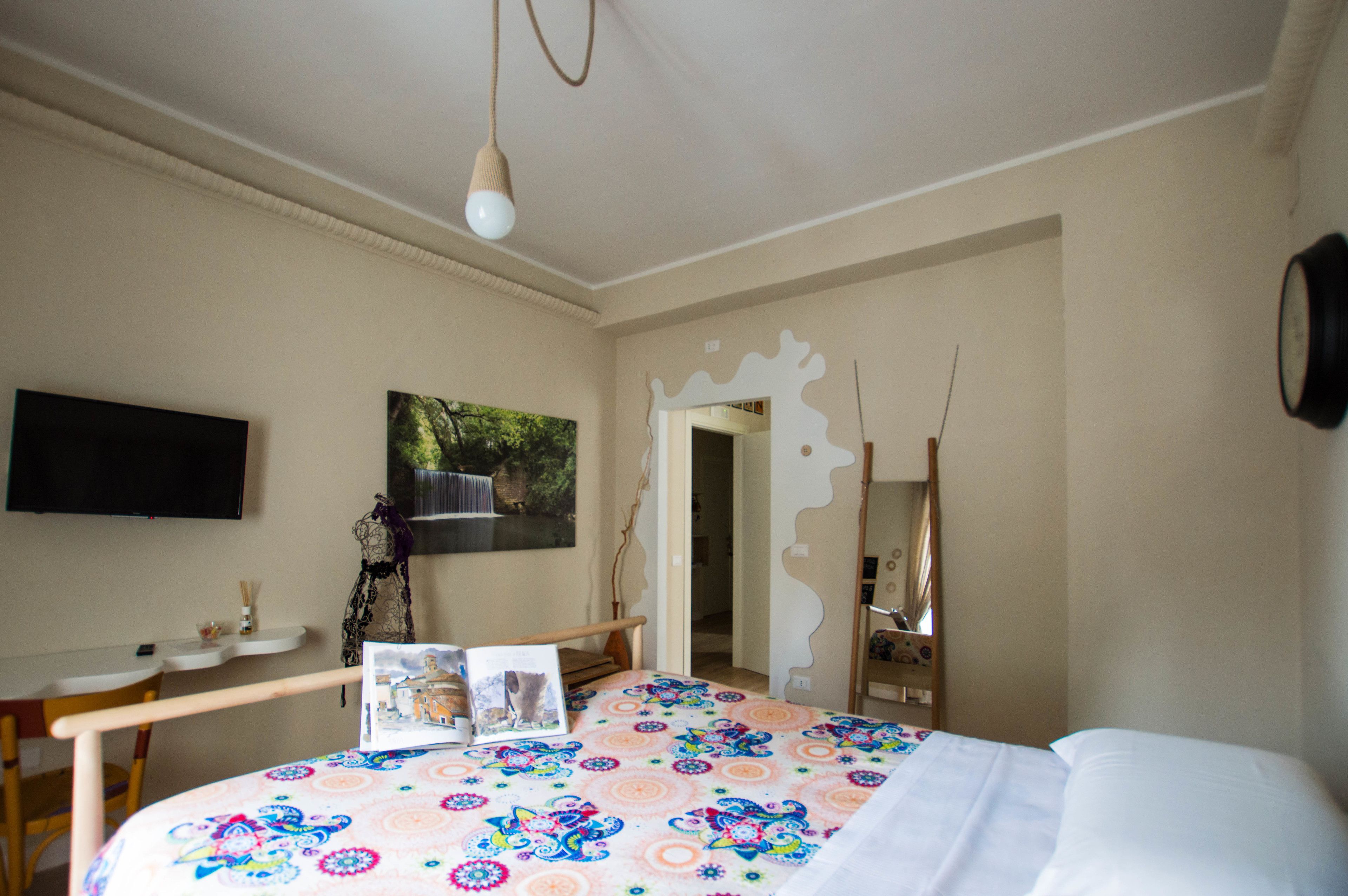 A bedroom with a bed, a desk, a chair, a TV, and a painting on the wall.