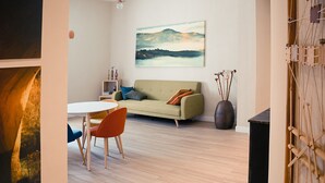 A modern living room with a sofa, a round table, and chairs. There is a painting on the wall and a vase with sticks. - Leucos B&B (Potenza)