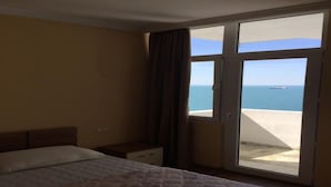 Ein Hotelzimmer mit Bett, Nachttisch, einem Fenster mit Vorhängen und Meerblick.