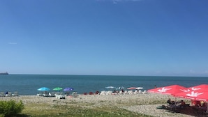 Ein Strand mit Liegestühlen und Sonnenschirmen, ein Schiffen in der Ferne und einem wolkenlosen, blauen Himmel.