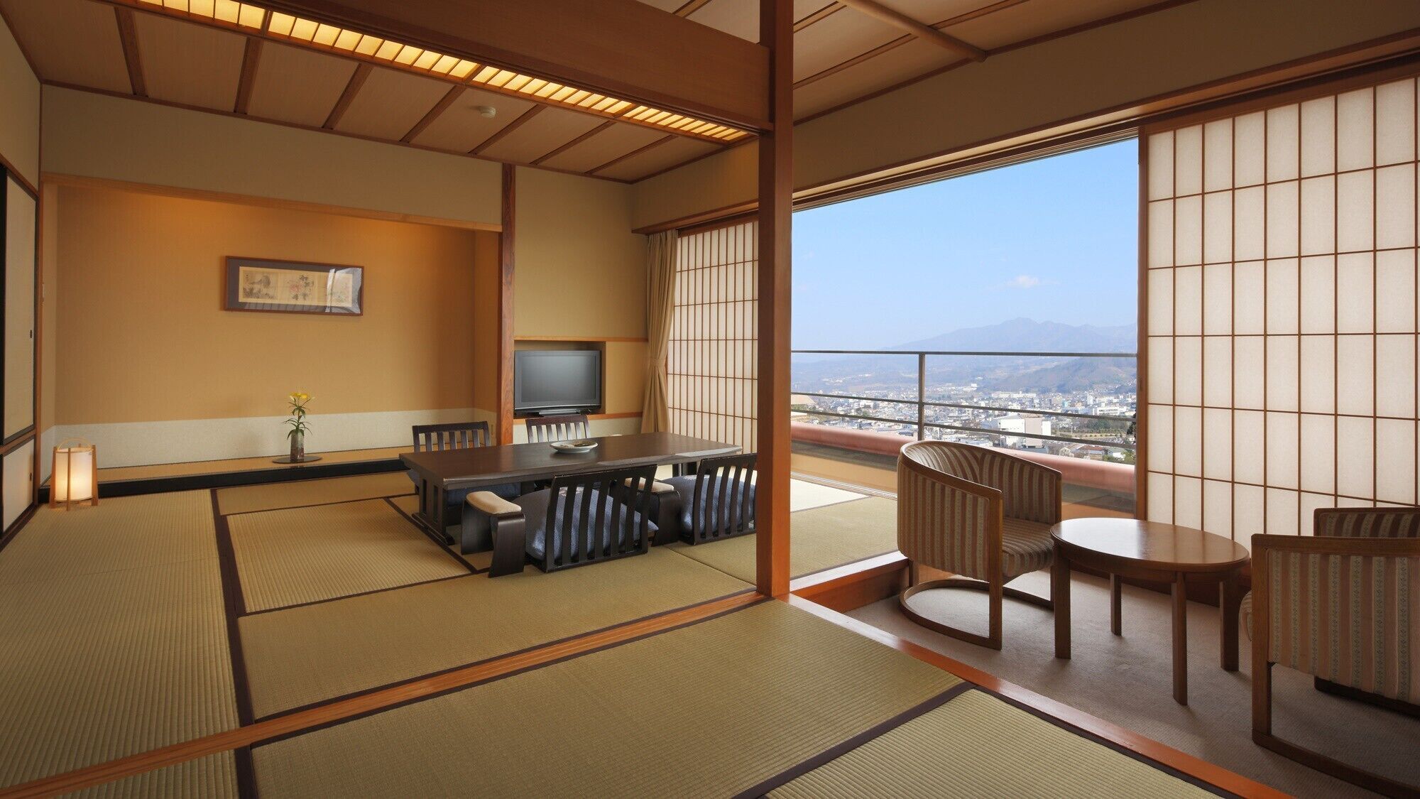 Et traditionelt japansk værelse med tatamimåtter, et fjernsyn og en balkon med udsigt over byen.