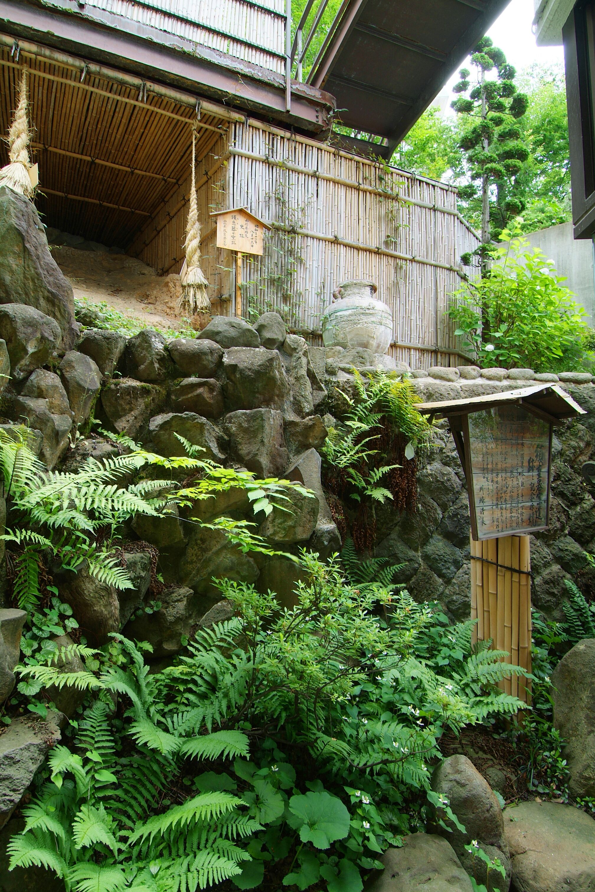 Ein traditioneller japanischer Garten mit Bambuskonstruktion, Steinmauern und üppiger Vegetation.