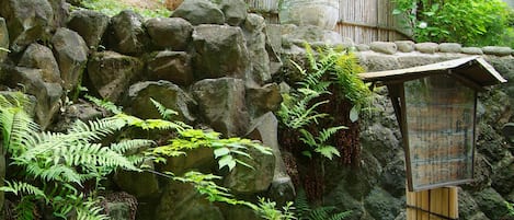 A traditional Japanese garden with a bamboo structure, stone walls, and lush greenery.