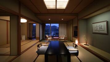 Una habitación tradicional japonesa con suelo de tatami, una mesa baja y sillas. Hay un ventanal con vistas a montañas.