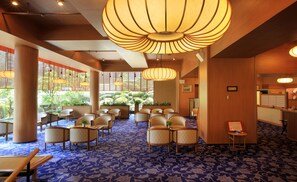 Um hall de hotel com carpete padronado em azul, cadeiras de madeira e grandes lustres.