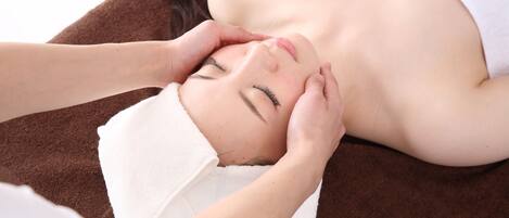 A person lying on a brown surface with a white towel, receiving a facial treatment.