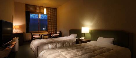 A hotel room with two beds, a desk, a chair, and a TV.