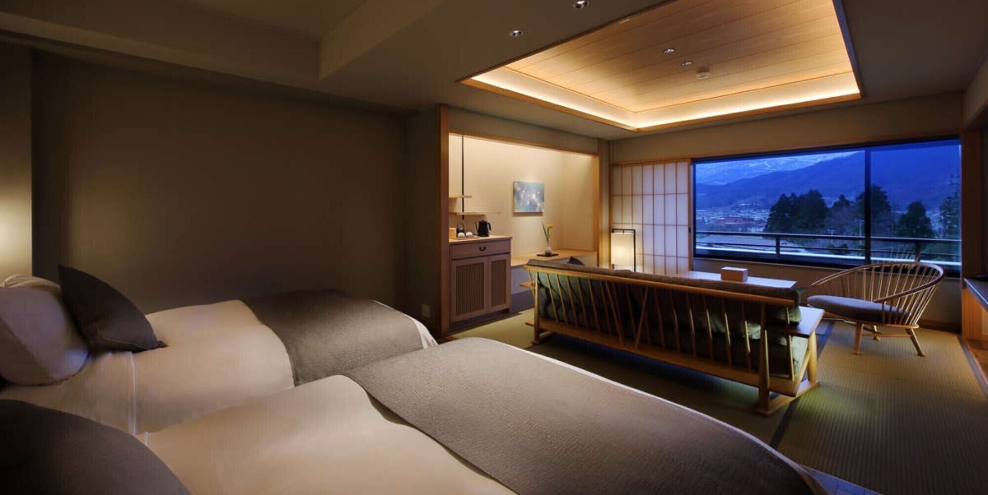 A modern hotel room with a sofa, a small table, a chair, a view of the outdoors, and a traditional Japanese sliding door.