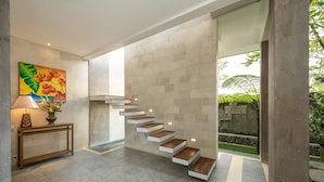 A modern interior with a staircase, a console table with a vase, and a painting on the wall. - Prabhu Ubud Villa (Ubud)