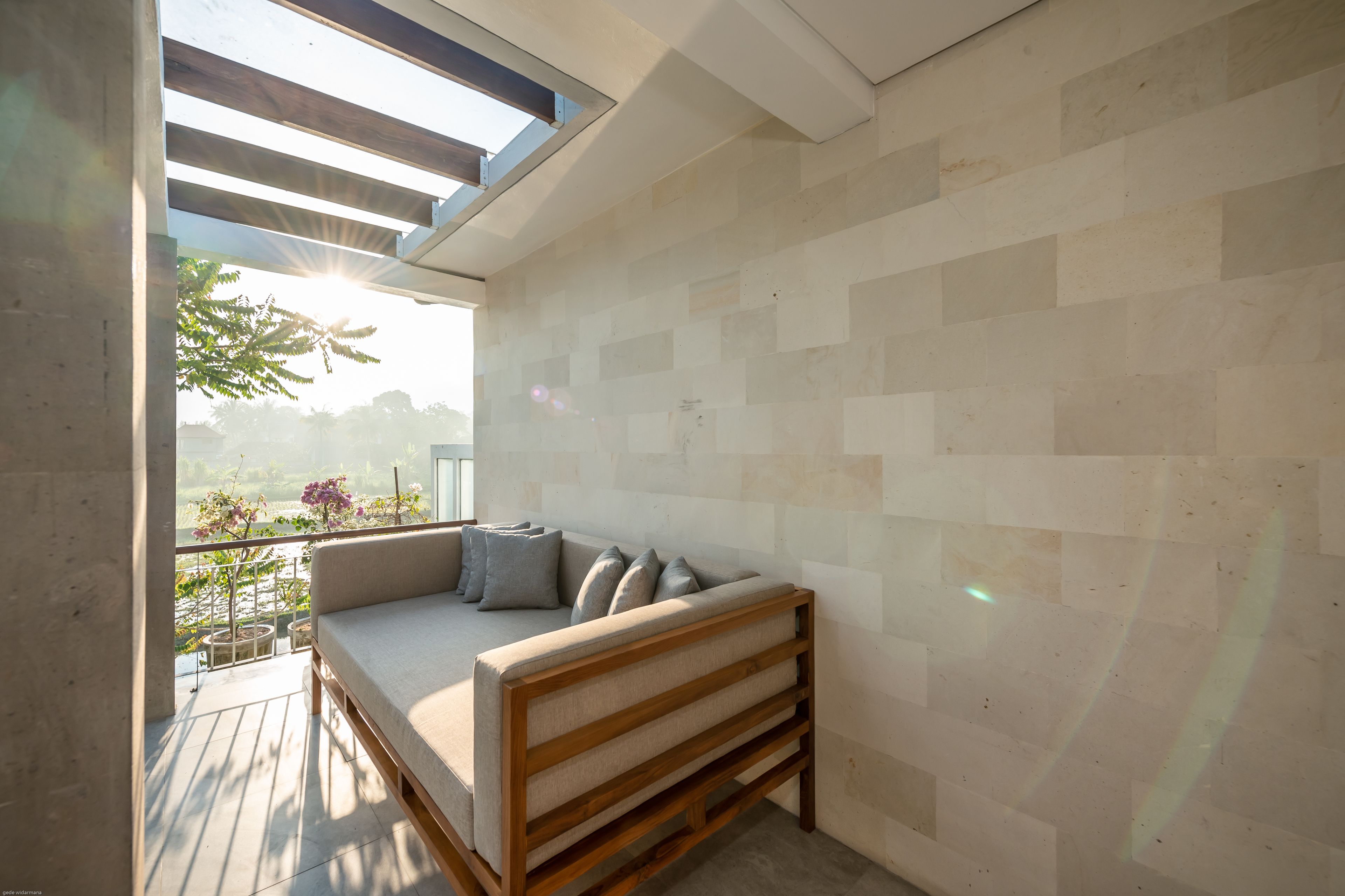 A modern balcony with a wooden bench and cushions, a tiled wall, and a view of greenery.