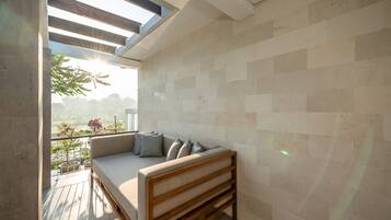 A modern balcony with a wooden bench and cushions, a tiled wall, and a view of greenery.