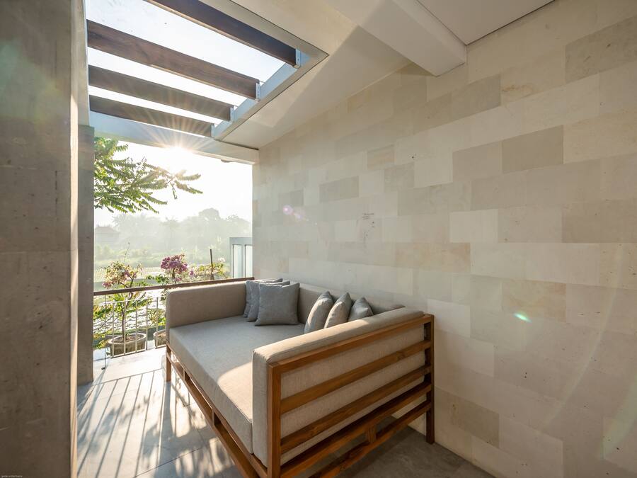 A modern balcony with a wooden bench and cushions, a tiled wall, and a view of greenery.