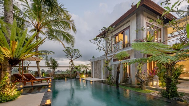 A swimming pool with lounge chairs, surrounded by tropical plants and a two-story building with balconies. - Prabhu Ubud Villa (Ubud)