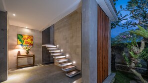 A modern staircase with a wooden finish, a wall-mounted painting, and a small table with a lamp and flowers. - Prabhu Ubud Villa (Ubud)