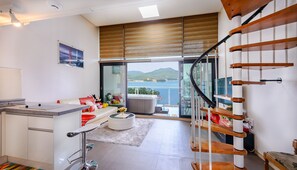 A modern kitchen with a large window, a dining area with a white table and red chairs, and a spiral staircase. - Tongyeong Honey Spa Pension (Tongyeong)
