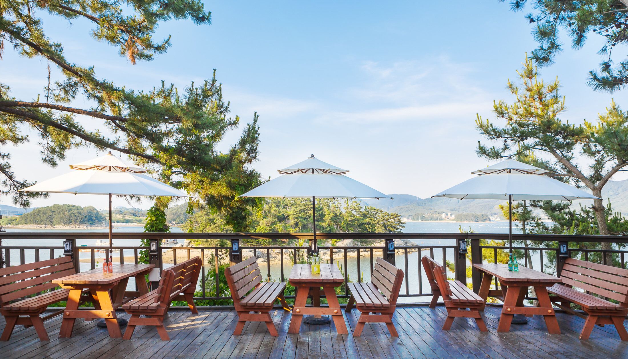 A deck with wooden benches and picnic tables, overlooking a body of water with mountains in the background.