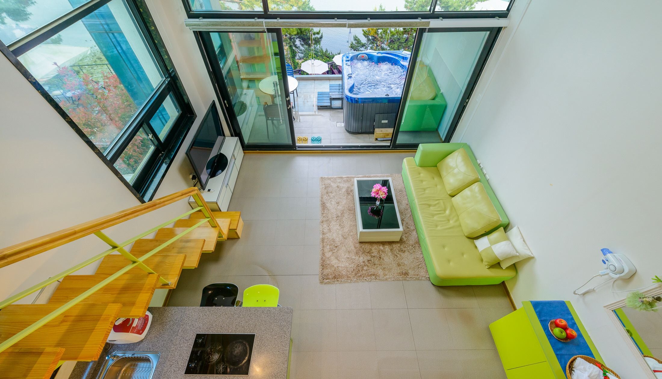 A modern interior with a staircase, a green sofa, a coffee table, and a hot tub visible through a glass door.