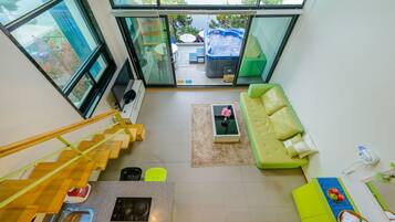 A modern interior with a staircase, a green sofa, a coffee table, and a hot tub visible through a glass door.