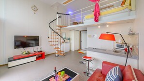Un salon moderne avec un téléviseur, un canapé rouge, un coin repas avec une lampe rouge et un escalier.