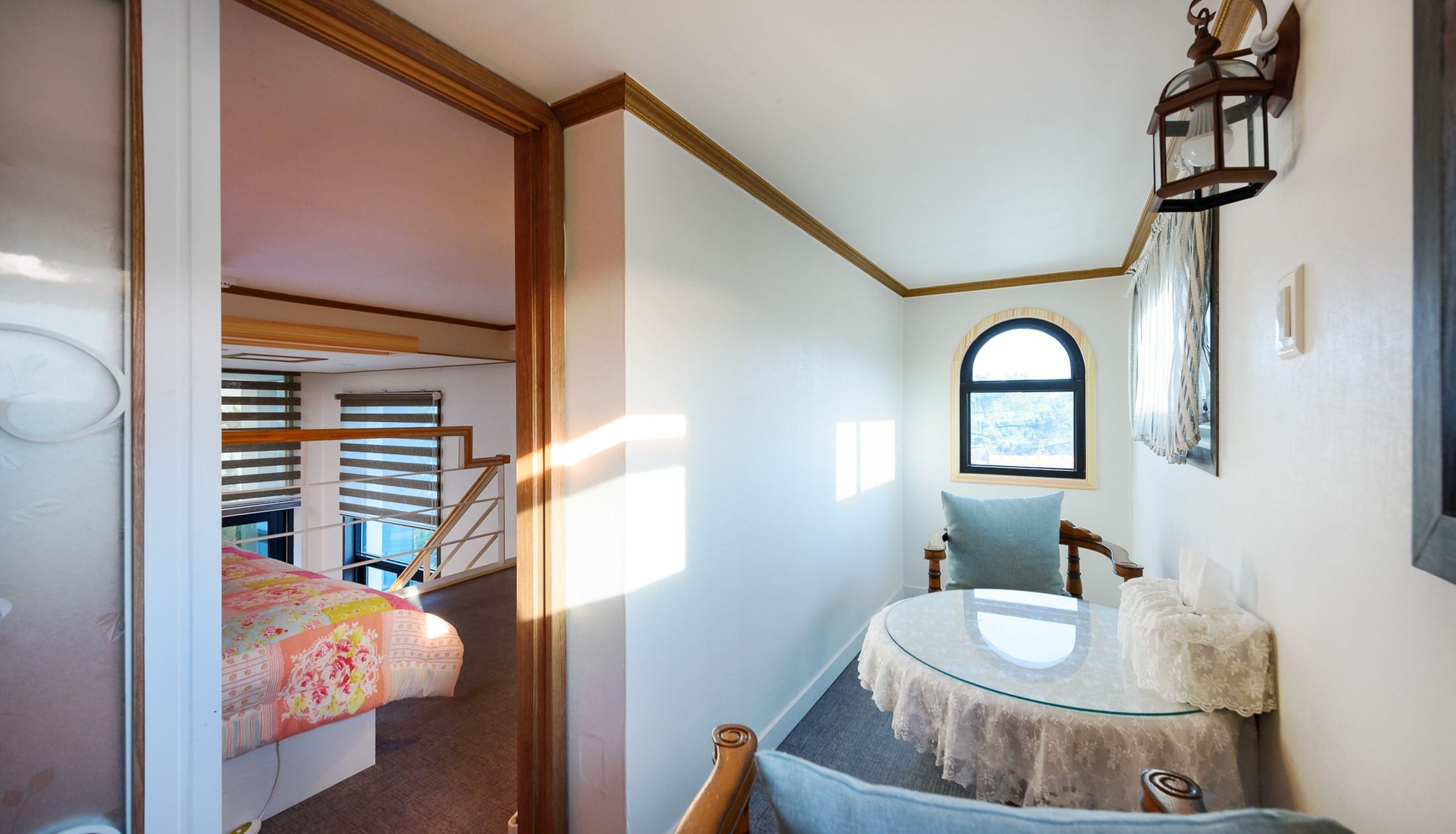 A bedroom with a bed, a round glass table, a chair, a window, and a staircase.