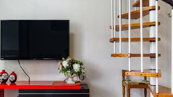 A living room with a flat-screen TV mounted on the wall, a wooden chair, a small table with a vase of flowers, and a red bench.