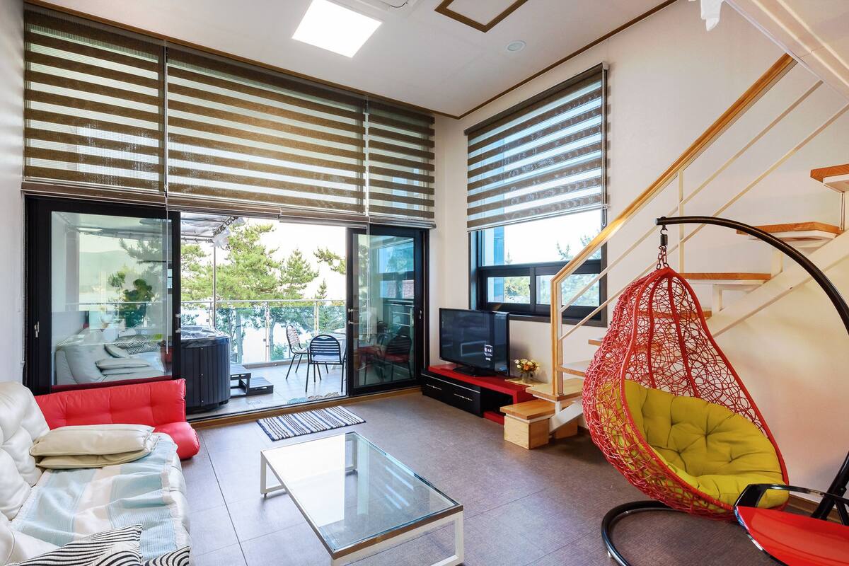 A modern living room with a sofa, a glass coffee table, a hanging chair, and a TV.