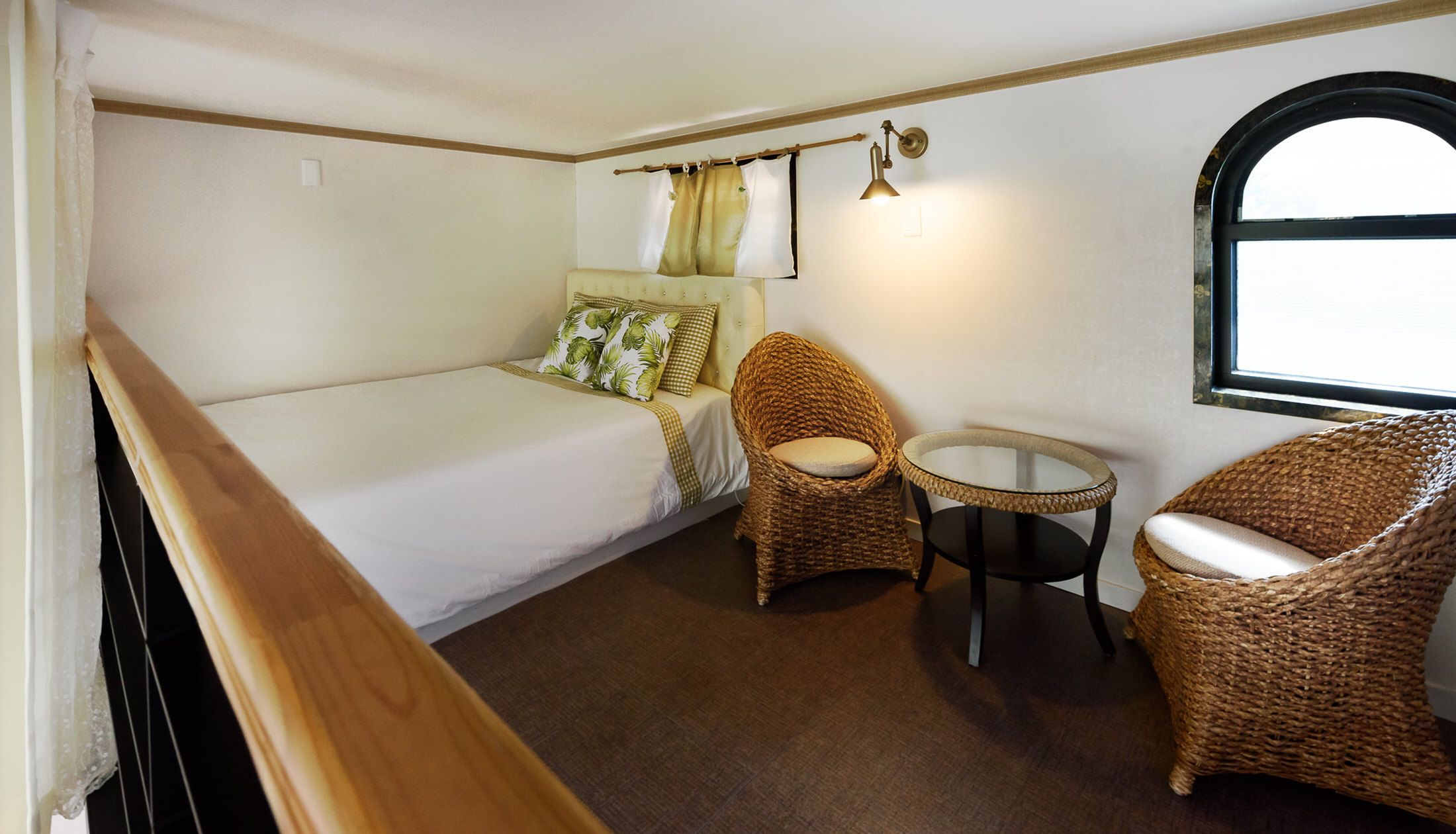 A compact room with a bed, two wicker chairs, a small round table, and a window with curtains.
