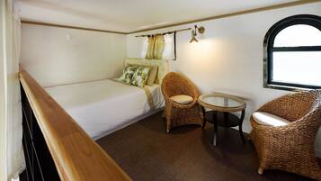 A compact room with a bed, two wicker chairs, a small round table, and a window with curtains.