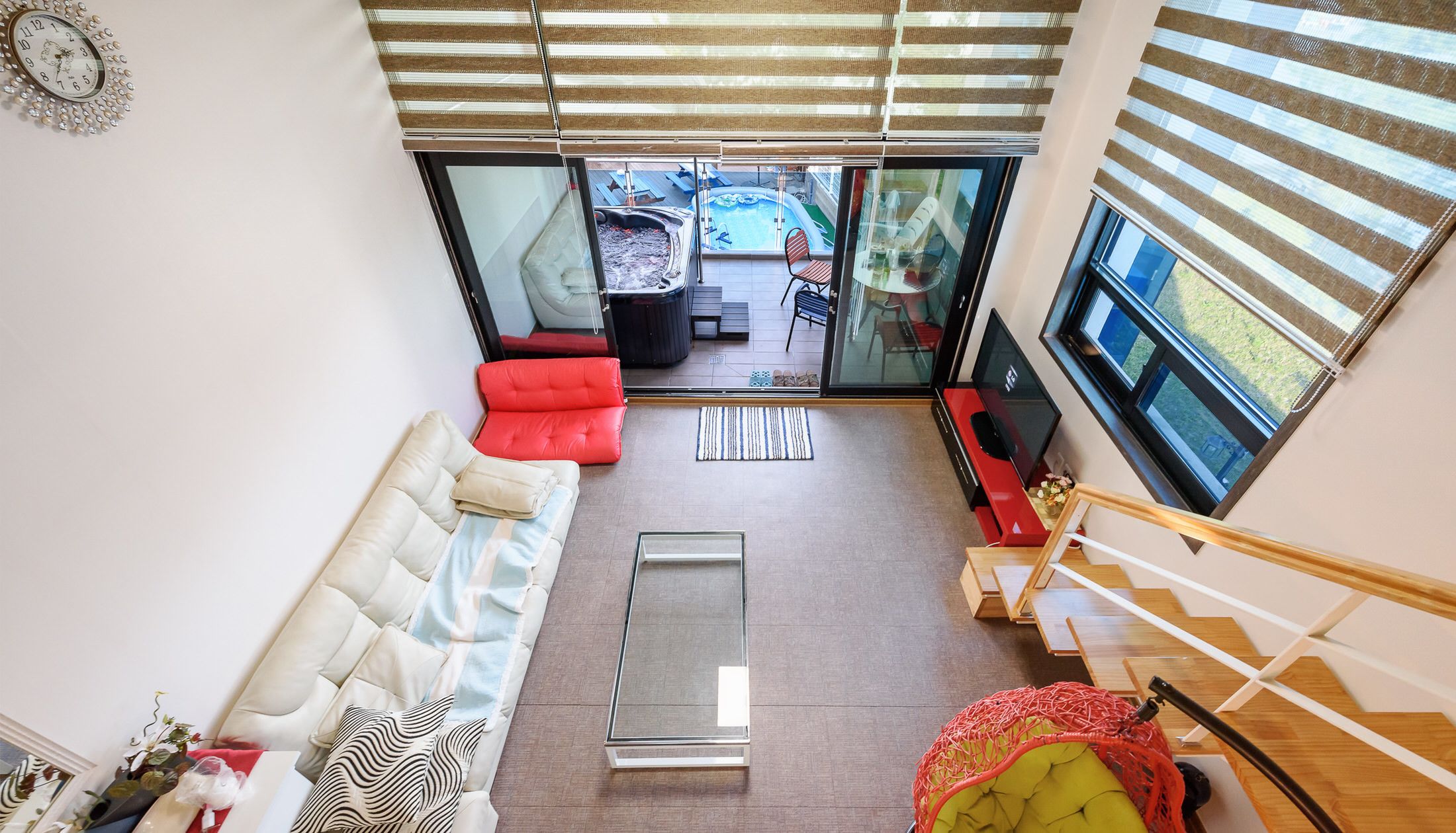 A modern living room with a sofa, a red chair, a glass coffee table, and a TV.