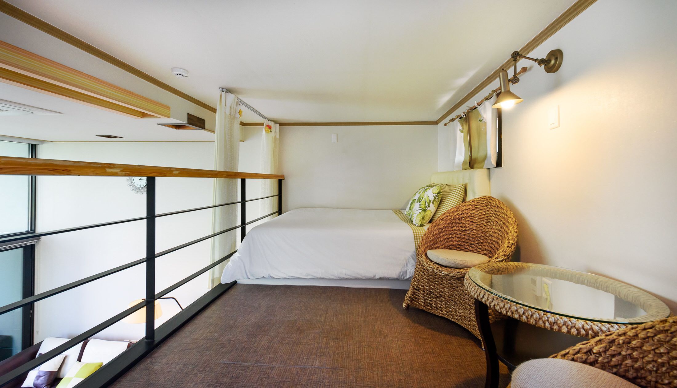 Habitación de hotel pequeña con cama, una silla de mimbre, una mesita y vistas por la ventana.