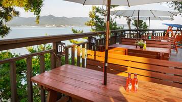 An outdoor dining area with wooden tables and benches, overlooking a body of water and hills.