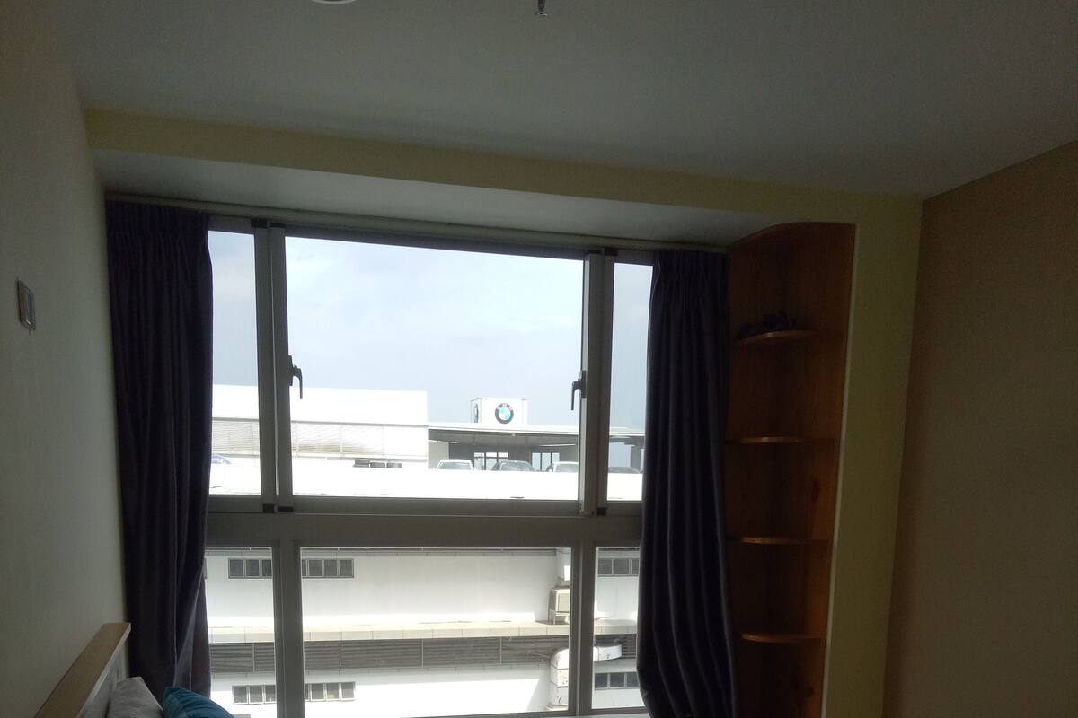 Habitación de hotel con cama, ventana con cortinas, armario de madera y vista a edificios.
