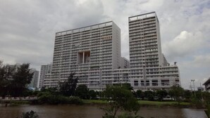 A high-rise building with multiple floors, surrounded by greenery and a body of water.
