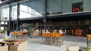 An indoor dining area with tables and chairs, large windows, and a view of buildings outside.