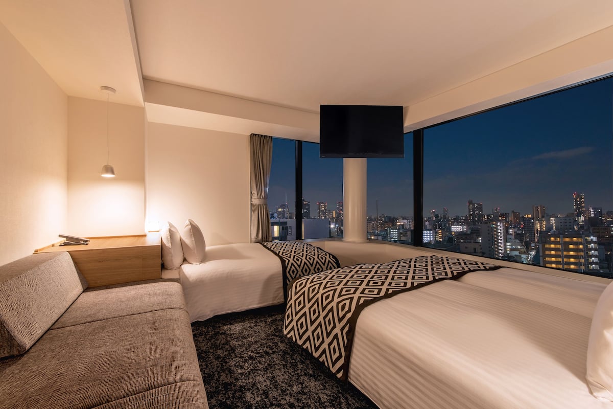 Ein Hotelzimmer mit Blick auf die Stadt, inklusive Sofa, zwei Betten, einem Flachbildfernseher und einem Nachttisch mit Lampe.