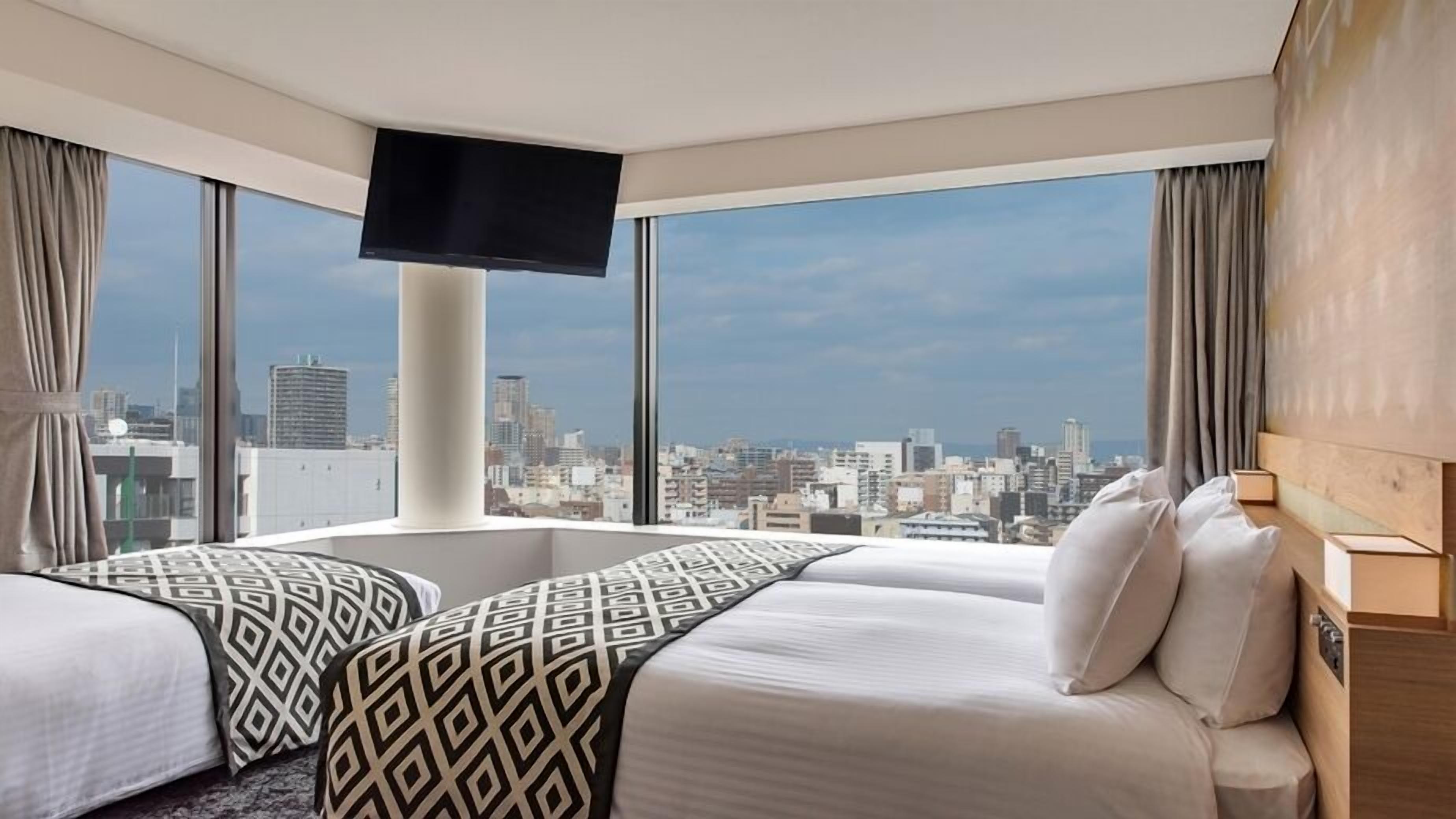 Une chambre d’hôtel avec vue sur la ville, une télévision à écran plat et un lit agrémenté d’oreillers à motifs.