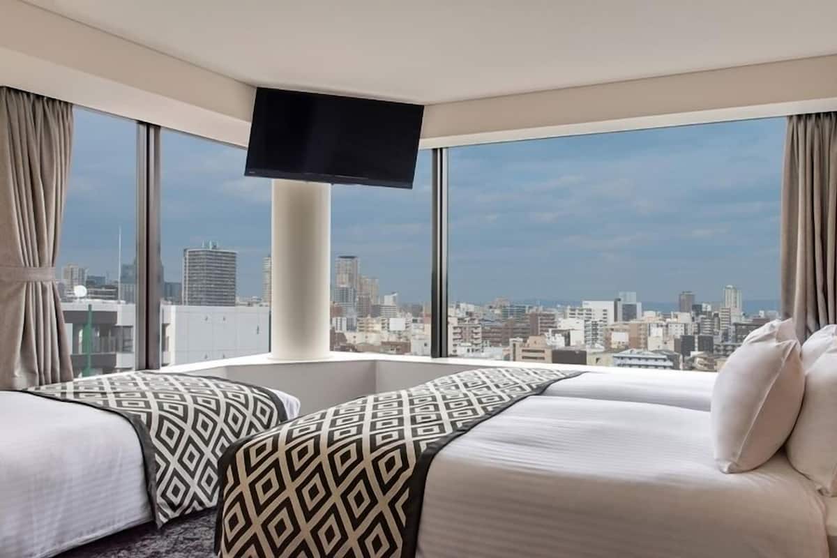 Ein Hotelzimmer mit Stadtblick, einem Flachbildfernseher und einem Bett mit gemusterten Kissen.