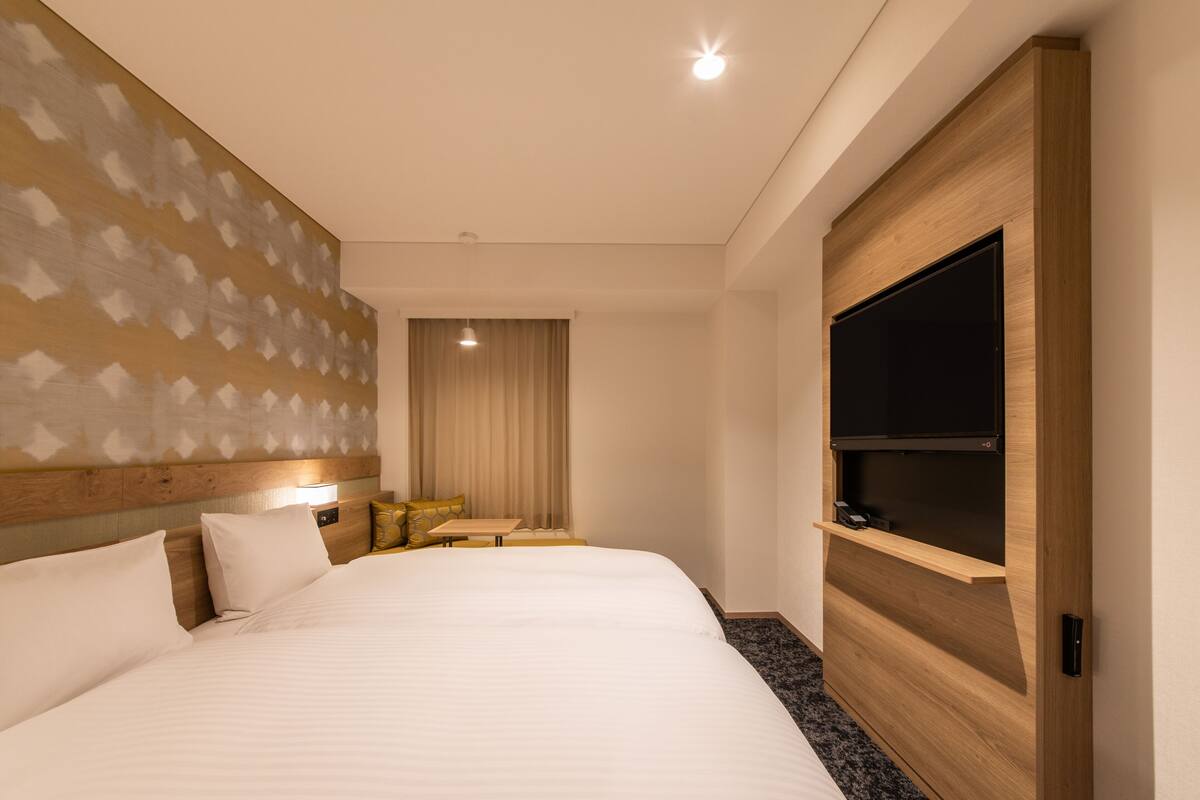 Ein Hotelzimmer mit einem großen Bett, einem Holzkopfteil, einem Flachbildfernseher, einem kleinen Tisch und einer Sitzecke mit einem Sessel und einer Lampe.