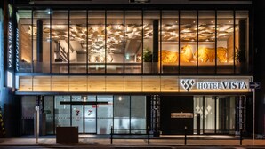 Un hôtel au design moderne, doté d’une entrée imposante avec des portes en verre et d’une enseigne indiquant « HÔTEL VISTA ».