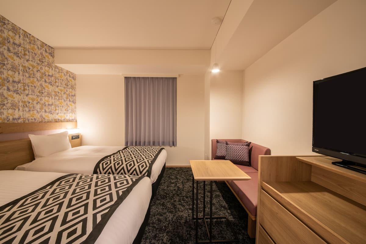 Ein Hotelzimmer mit zwei Betten, einem Schlafsofa, einem Fernseher und einem kleinen Tisch.