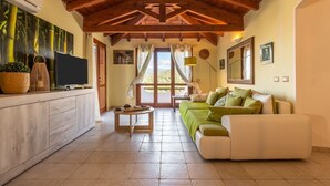A spacious living area with a wooden ceiling, a sofa set, a TV, and a dining table. - Villa Camelia panoramic villa facing the sea (Torre Delle Stelle (Maracalagonis))