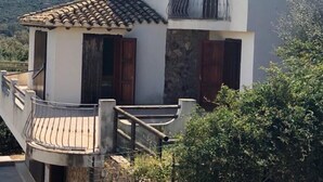A two-story building with a tiled roof, stone facade, and a balcony with a metal railing. - Villa Camelia panoramic villa facing the sea (Torre Delle Stelle (Maracalagonis))